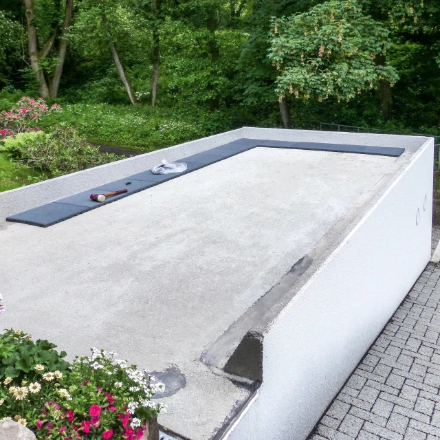 Tegenover weelderig groen ligt een garage die in de helling is gebouwd, vermoedelijk voor een woonhuis. Op het betonnen dak worden leigrijze terrastegels van WARCO gelegd, zodat het dak in de toekomst als terras kan worden gebruikt.