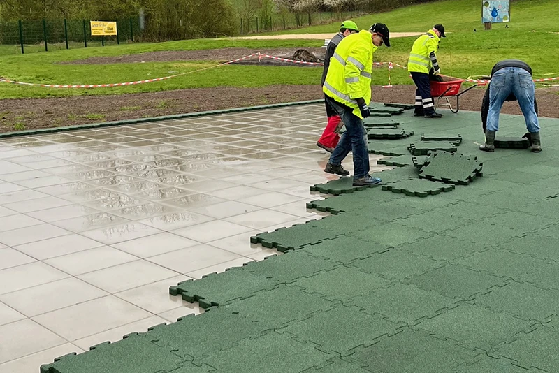 Een groep arbeiders die groene WARCO Outdoor-kliktegels in de regen leggen op een betegelde buitenruimte.