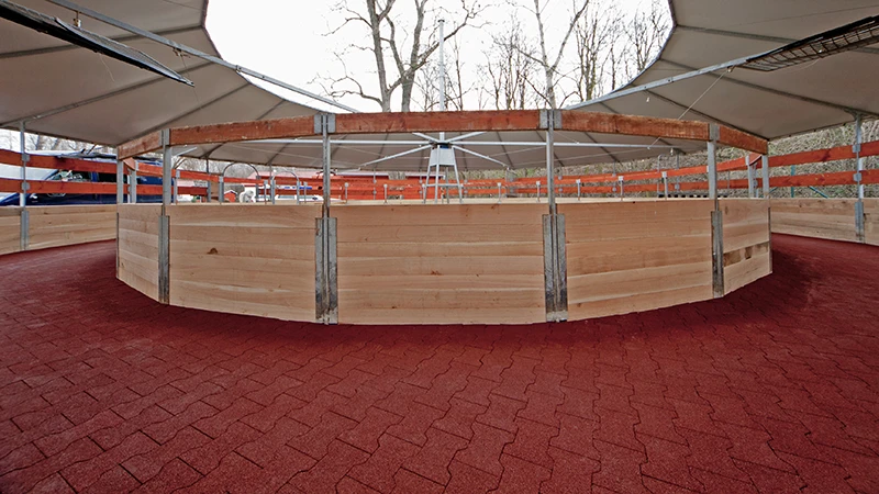 De foto toont een moderne, overdekte stapmolen voor paarden. Het looppad is volledig bestraat met rode rubberen verbindingsstenen – slipvast, waterdoorlatend en gewrichtsvriendelijk. Het elastische oppervlak zorgt voor veilige beweging van de paarden bij elk weer en in elke gang. Het stabiele pad vereist weinig onderhoud. De installatie is ideaal voor maneges, fokstallen en paardenklinieken die waarde hechten aan diervriendelijke bodems, weinig werk en duurzaam materiaal.