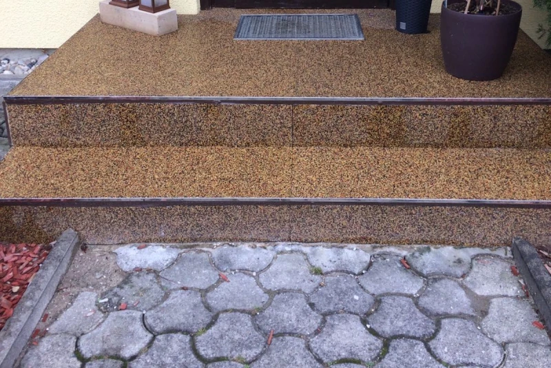 Een bruine trap leidt twee treden naar de ingang van het huis. Ervoor liggen grijze beenderstenen.