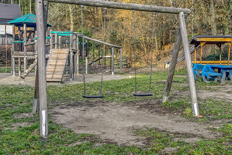 Twee schommels hangen troosteloos boven een stuk aarde. Er zijn resten van gras te zien. De schommels zien er allesbehalve uitnodigend uit.
