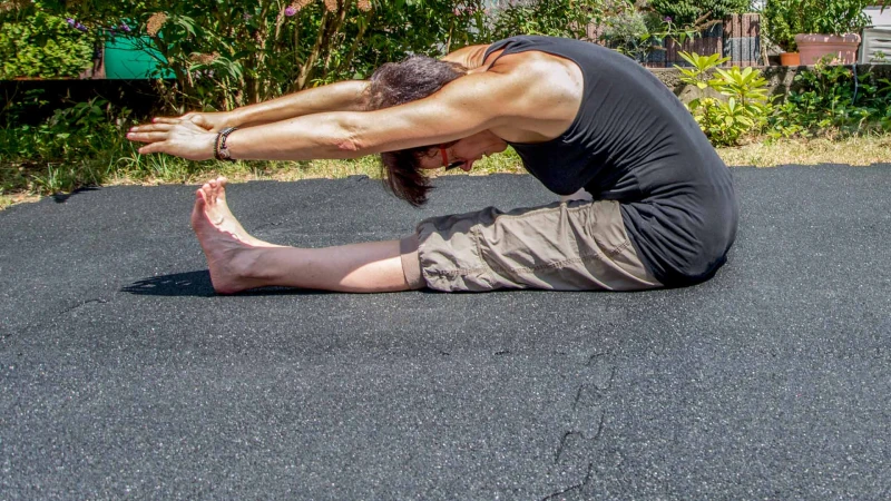 Een vrouw doet rekoefeningen op een antracietkleurige rubberen vloer gemaakt van WARCO fitnessplaten. De fitnessruimte bevindt zich in de tuin, in het gazon.