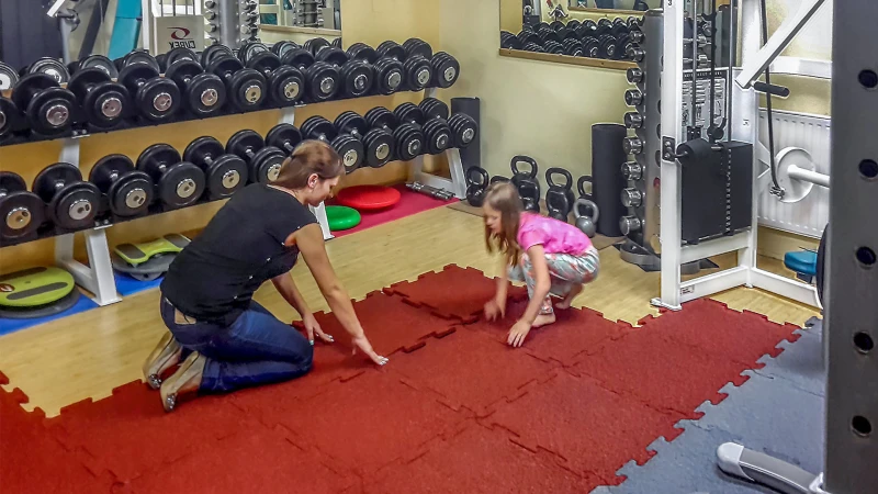Moeder en dochter leggen de handige fitnessborden in baksteenrood of licht beton in de fitnessruimte thuis. Tegen de muur staan halters en apparatuur voor krachttraining.