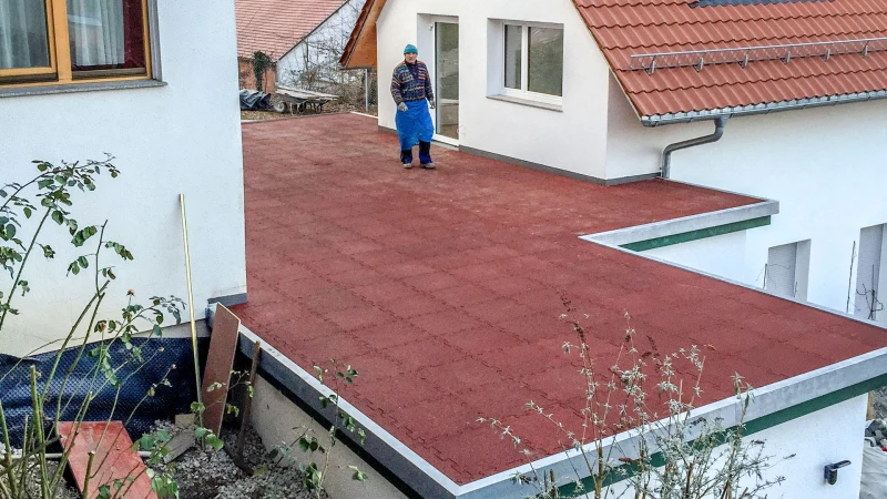 Twee woongebouwen staan op een perceel op een heuvel. Tussen de huizen werd een garage-uitbouw geplaatst. Het platte dak op de garage-uitbouw werd door de bewoners van het huis zelf ontworpen tot een dakterras met behulp van WARCO-terrastegels.