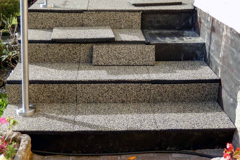 Een betonnen trap naar een verhoogd terras is bekleed met WARCO trapbekleding. Op de laatste trede ontbreken nog drie elementen, maar die zijn al op maat gezaagd en klaar om in de volgende stap te worden vastgelijmd.