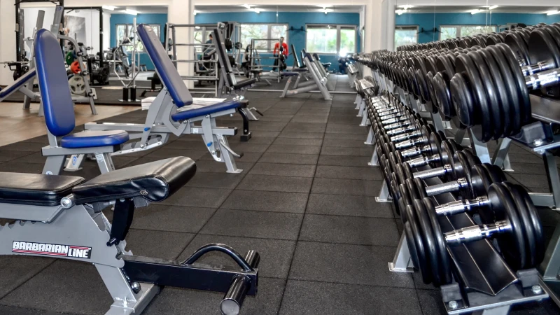 In een sportschool staan verschillende schuine banken opgesteld voor haltertraining op een goed gepolsterde vloer van WARCO Fitness. Voor de schuine banken staat een plank met halters klaar om te trainen.
